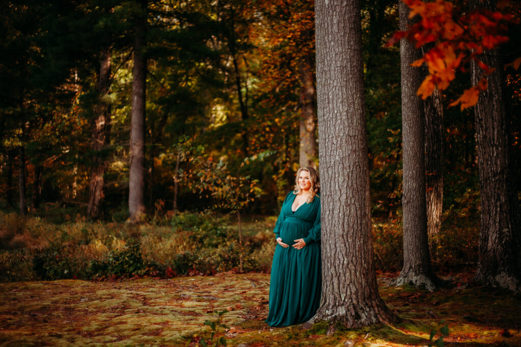 pregnant mother poses next to tree in lush autumn forest